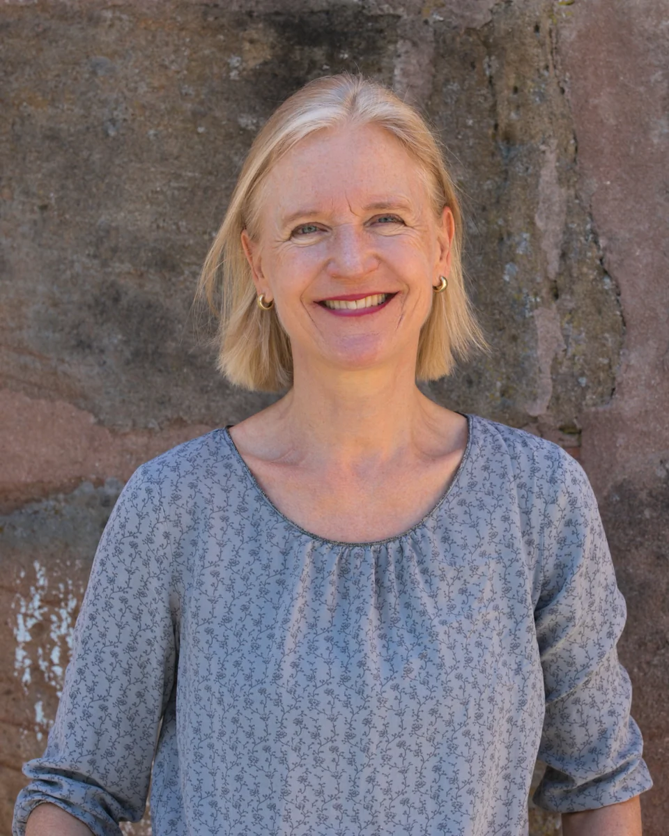 Britta Ernst lächelt zugewandt vor einer Sandsteinmauer