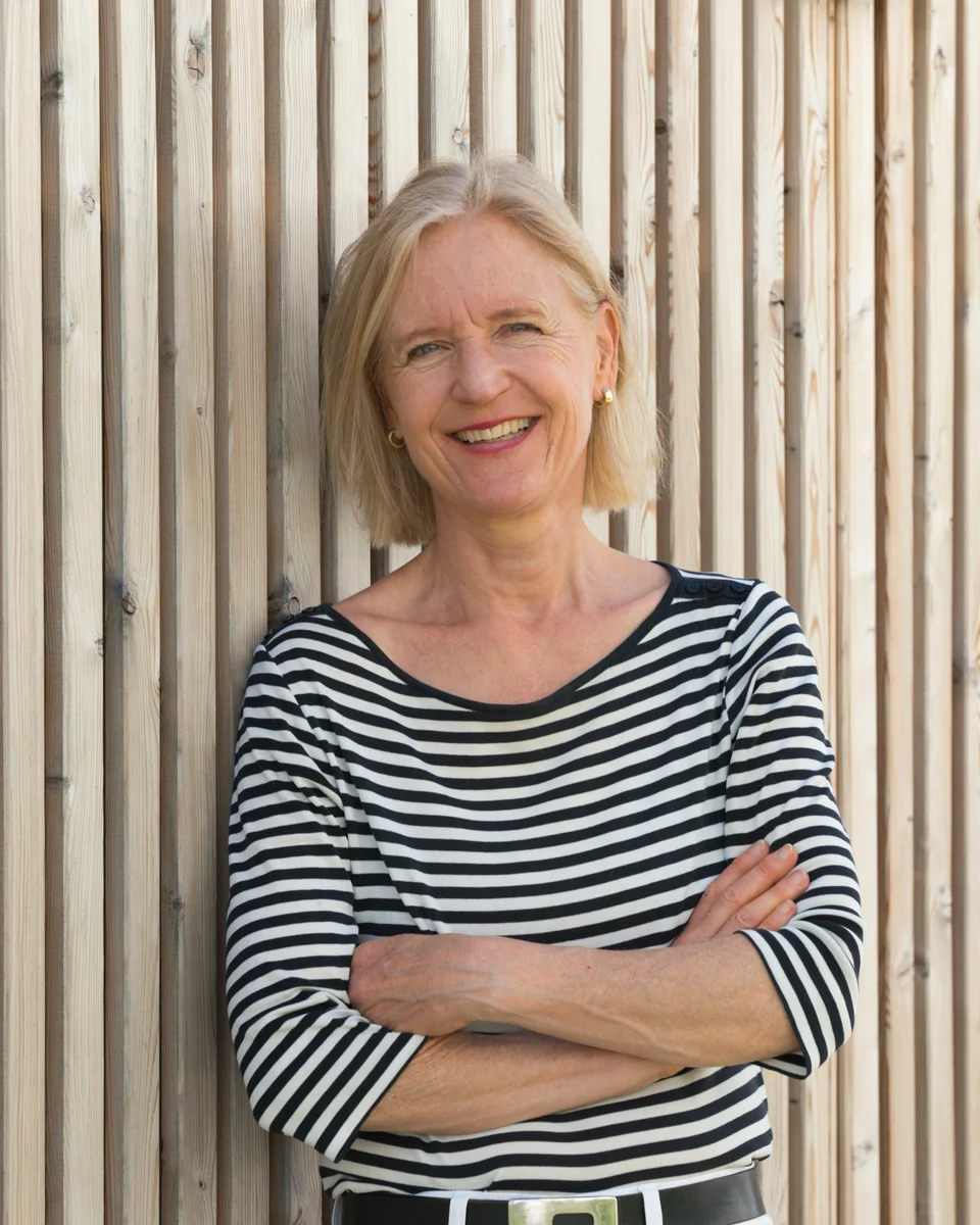 Britta Ernst lehnt mit verschränkten Armen lächelnd an einer Holzwand